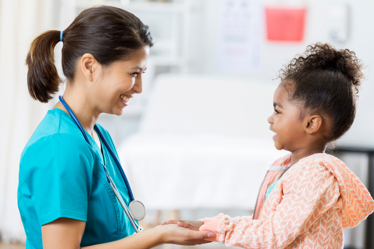 Pediatric nurse and child face each other holding hands
